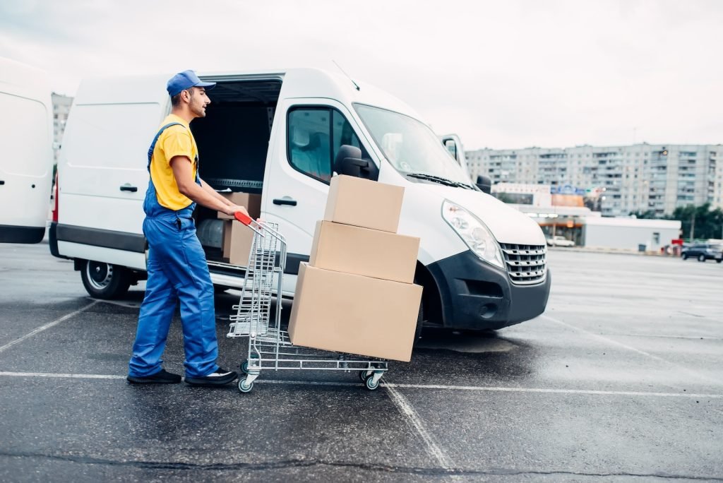 6523d1655c1a2b5a1ef544d4-courier-with-parcel-trolley-against-logistic-truck-2021-08-26-16-25-49-utc